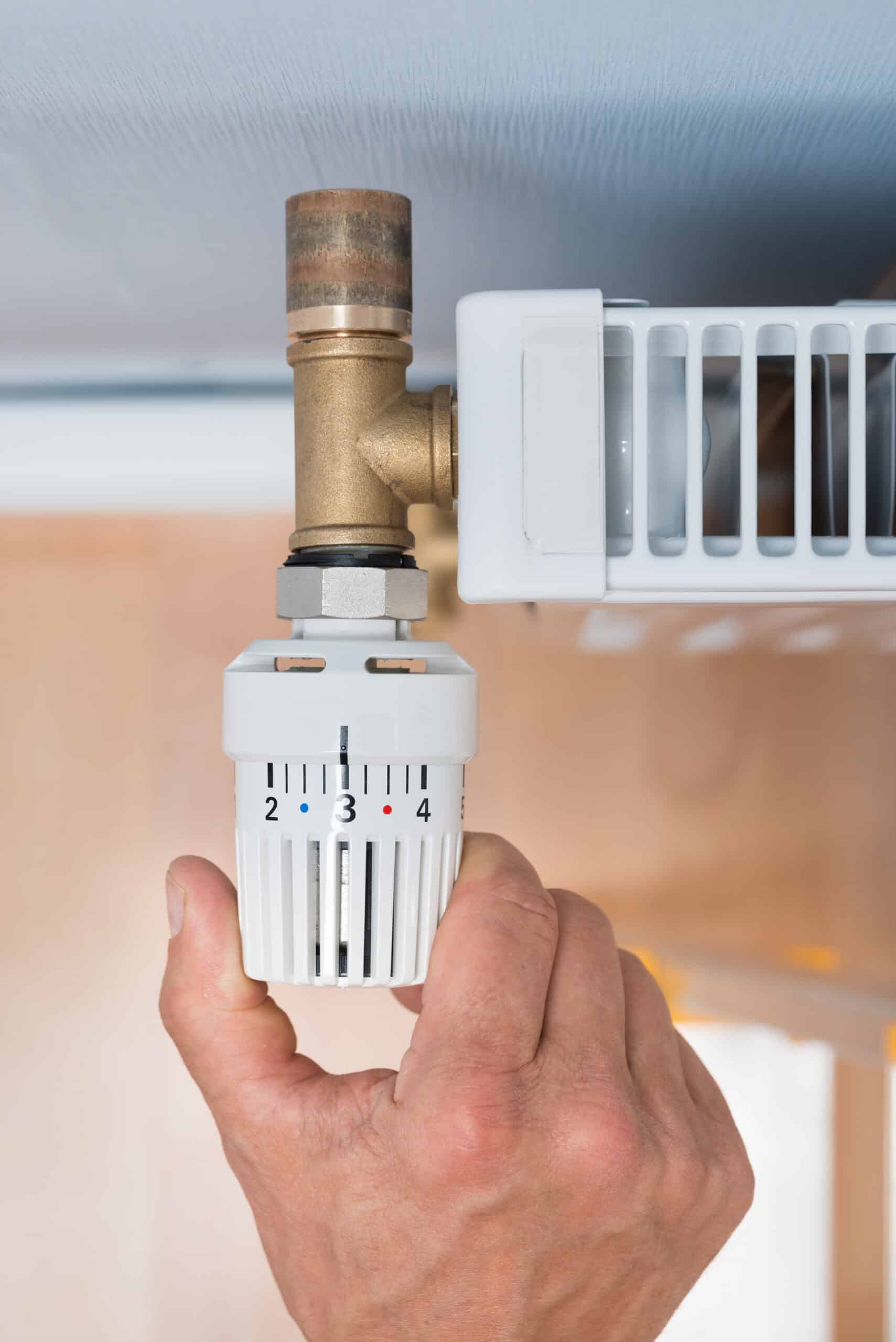 Main ajustant un robinet thermostatique de radiateur blanc, réglé sur 3 (points bleu/rouge visibles). Nombres 2, 3, 4 affichés.