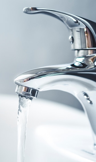 Gros plan d'un robinet de salle de bain chromé moderne avec un jet d'eau clair coulant dans un lavabo blanc.