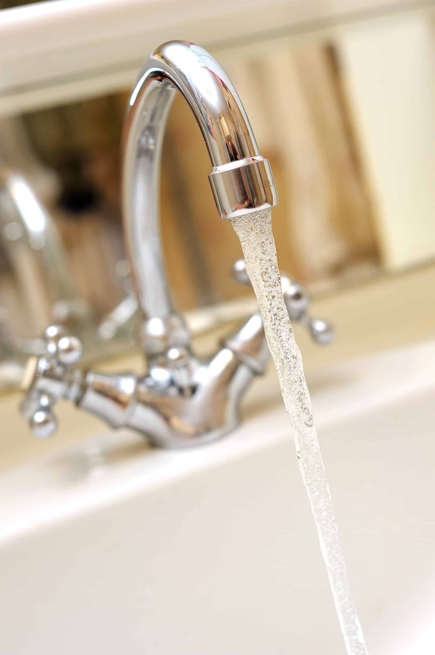 Robinet chromé brillant avec de l'eau claire et mousseuse qui coule dans un lavabo blanc. Arrière-plan flou de salle de bain.