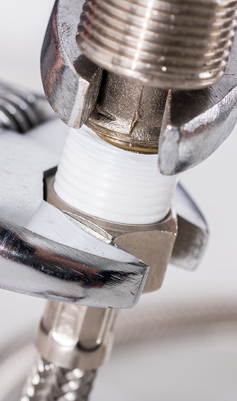 Closer sur une clé à molette serrant un raccord de plomberie, avec filetage et ruban PTFE blanc visible.